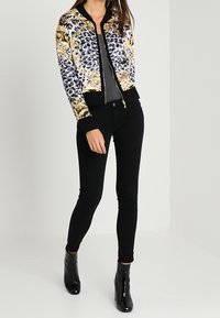 Bomberjack met een kleurrijk bloemen- en luipaardprintpatroon, zwarte geribbelde manchetten en zoom, gecombineerd met aansluitende zwarte jeans en enkellaarsjes.