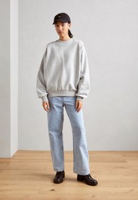 Sudadera gris de gran tamaño con puños y dobladillo acanalados, combinada con jeans rectos de color azul claro y botas de tacón negro hasta el tobillo. Gorra negra.