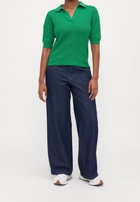 Grön ribbad stickad polotröja med korta ärmar, kombinerad med löst sittande mörkblå denimjeans och vita sneakers med bruna sulor.