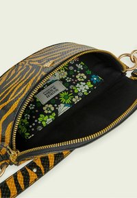 Sac bandoulière rayé noir et orange avec une fermeture éclair dorée, doté d'un intérieur à motif floral et d'une étiquette de marque intérieure.