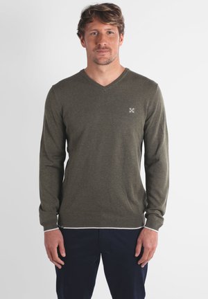 Pull v-neck vert olive en maille douce avec des manches longues, présentant un ourlet à rayures blanches et un petit logo sur la poitrine.