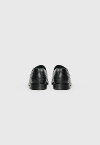 Zwarte leren schoenen met een glad oppervlak, ronde neus, lage hak en decoratieve stiksels aan de achterkant. Groene voering is zichtbaar aan de binnenkant.