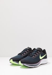 Mustat urheilukengät, joissa on teksturoitu päällinen, vihreät korostukset pohjassa ja heijastava Nike-logo. Varustettu hengittävällä verkkosuunnittelulla.