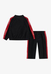 Black tracksuit featuring a zip-up jacket and elastic waistband pants. Red accents with "JORDAN" logo on sleeves and pants sides. Smooth fabric.