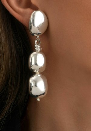 Boucles d'oreilles en argent avec trois grandes perles rectangulaires arrondies portées sur l'oreille d'une personne avec des cheveux bruns visibles.