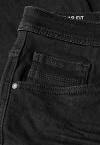 Primer plano de unos vaqueros de mezclilla negros que muestran el bolsillo frontal, el pequeño bolsillo para monedas, los detalles de las costuras y el remache de metal.