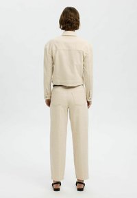 Beige denim jack en wijdgevallen broek met strakke lijnen en een minimalistisch ontwerp. Achterzakken op de broek, knopen op de manchetten van de jack.