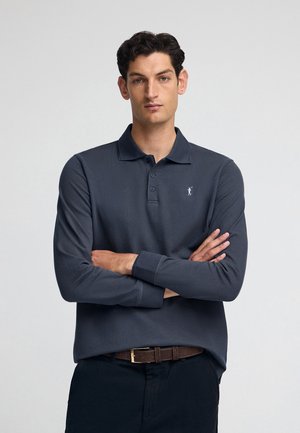 Polo a maniche lunghe blu navy con colletto, dotato di una placca con tre bottoni e un piccolo logo sul lato sinistro del petto. Texture liscia, vestibilità casual.