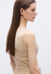 Camiseta sin mangas beige con diseño ajustado y estilo sin mangas, con cuello redondo y tela texturizada. Acabado suave y delicado.