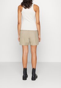 Shorts beige avec des ourlets retroussés, associés à un débardeur blanc et des bottines noires. Le tissu semble doux avec un design décontracté.