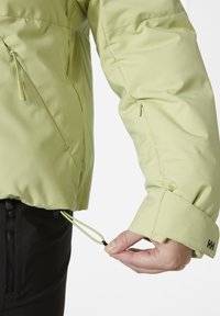 Hellgrüne isolierte Jacke mit Reißverschlüssen, Kordeln und verstellbaren Bündchen. Glatte Textur und praktisches Design für den Einsatz im Freien.