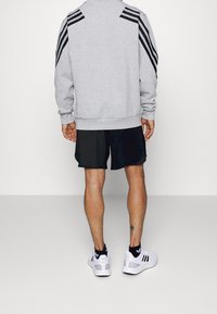 Grå sweatshirt med svarta ränder på axlarna, kombinerad med svarta shorts och vita sportskor med svarta detaljer.