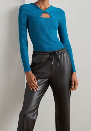 Haut à manches longues côtelé bleu canard avec une découpe en forme de clé, associé à un pantalon tapered en simili cuir noir avec une taille élastique et un cordon de serrage.