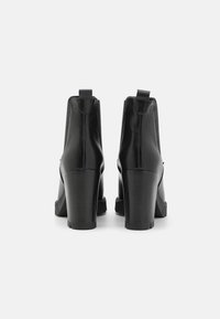 Botines de cuero negro hasta el tobillo con un alto tacón cuadrado, lengüeta para facilitar su uso y textura suave. Diseño minimalista sin herrajes o acentos visibles.