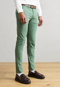Πράσινα chinos από ελαφρύ βαμβάκι, με στενή γραμμή, θηλιές για ζώνη και πλαϊνές τσέπες. Συνδυάζονται με καφέ loafers και λευκές κάλτσες.