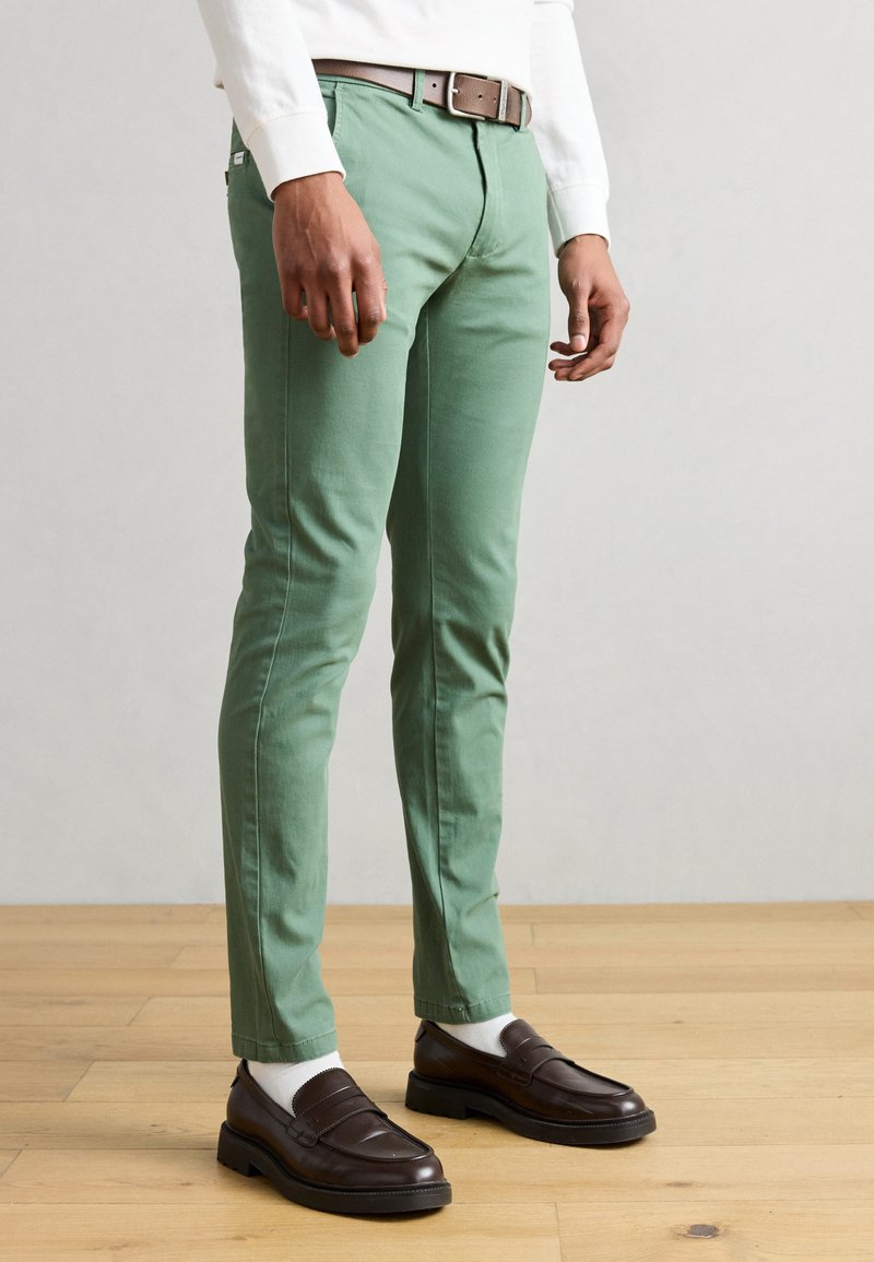 Πράσινα chinos από ελαφρύ βαμβάκι, με στενή γραμμή, θηλιές για ζώνη και πλαϊνές τσέπες. Συνδυάζονται με καφέ loafers και λευκές κάλτσες.