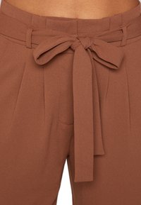 Bruine, high-waisted broek met een stoffen riem, voorzien van plooien en zijzakken. Glad textuur en op maat gemaakte pasvorm.