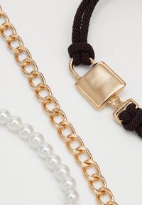Gold chain, pearl bracelet, and a brown rope with a gold lock. Features smooth and shiny textures, with varying thickness in chains.