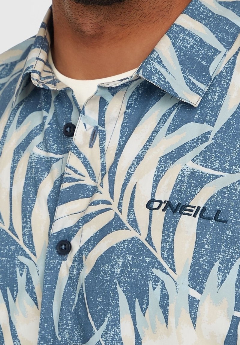 Gros plan d'une chemise à motifs bleu et blanc avec col, avec le nom de la marque brodé "O'Neill" sur la poitrine.