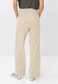 Pantaloni a gamba larga in beige chiaro con una sottile texture floreale e vita elasticizzata. Abbinati a scarpe argentate.