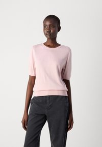 Light pink knitted sweater with short sleeves and ribbed hem; worn with dark gray pants. Soft texture and classic round neckline.