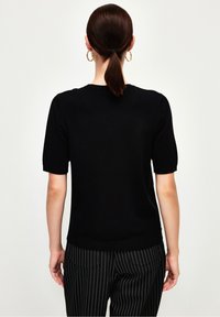 Černý krátký pletený top s kulatým výstřihem; hladká textura a přiléhavý střih. Kombinován s černobílými pruhovanými kalhotami.