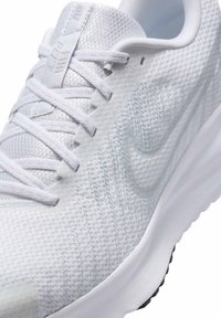 Gros plan d'une chaussure de course blanche Nike avec tissu tricoté, lacets blancs et un logo Swoosh subtil sur le côté.