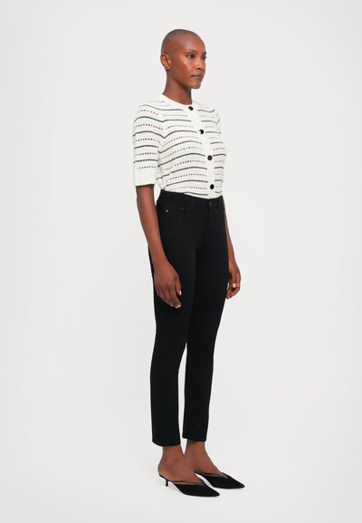 White short-sleeve cardigan with horizontal stripes and black buttons, paired with black fitted jeans and black kitten-heel shoes.