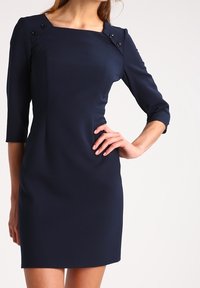 Mörkblå figursydd klänning med trekvartslånga ärmar, rutad halsringning och dekorativa knappar på axlarna. Slät, texturerad tyg.