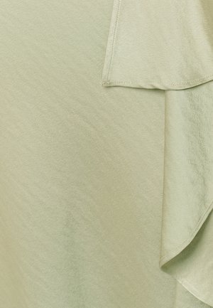 Zacht lichtgroen stof met overlappende lagen en zichtbare stikdetails op een glad textieloppervlak.