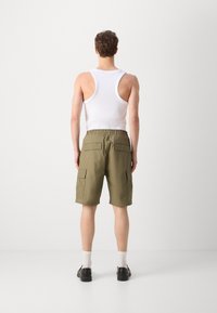 Shorts verzi din material cargo, cu un elastic la talie, buzunare laterale și la spate, și o croială lejeră, purtate cu un top alb fără mâneci și pantofi negri.