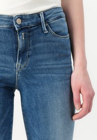 Blauwe denim jeans met een middelhoge taille, vijf zakken en een lichte vervaging. Voorzien van een knoop- en ritsluiting. Soepele textuur.