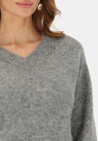 Jasnoszary sweter dzianinowy z dekoltem w serek i długimi rękawami; miękka faktura i lekko luźny krój; minimalistyczne wykończenie, odpowiedni do warstwowego stylu ubierania.