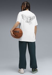 White t-shirt with an owl graphic on the back, paired with dark green pants. Includes a basketball with "PUMA" branding.