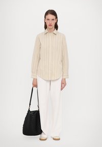 Beige stripete skjorte med knapper, hvite vide bukser og en teksturert svart vevet veske. Flate sko med en lett brun såle. Enkel, minimalistisk design.