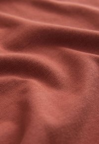 Gazdag terrakotta színű pamutszövet, finom bordázottsággal, lágy tapintással, enyhén redőzött és finom fényű.