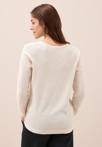 Beige Langarmpullover mit strukturiertem Strickdesign, rundem Halsausschnitt und seitlichen Schlitzen. Weiches Material fällt sanft. Keine sichtbaren Logos.