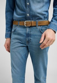 Denim hemd in medium blauw met een button-down kraag, gedragen met lichtblauwe jeans en een tan leren riem met een zilveren metalen gesp.