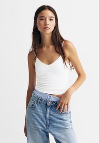 White, fitted sleeveless top with a V-neck design, paired with high-waisted light blue denim jeans featuring a striped waistband.