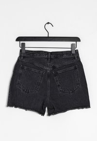 Schwarze Denim-Shorts mit ausgefranstem Saum, Fünf-Taschen-Design und Gürtelschlaufen, die an einem schwarzen Metallkleiderbügel vor einem weißen Hintergrund hängen.