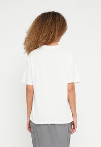 Λευκό κοντομάνικο μπλουζάκι με χαλαρή εφαρμογή και στρογγυλή λαιμόκοψη. Το ύφασμα φαίνεται μαλακό, με λείο υφή και ελάχιστες σχεδιαστικές λεπτομέρειες.