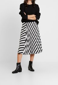 Svart tröja med långa ärmar, i kombination med en plisserad midi-kjol i växelvisa svarta och vita diagonala ränder. Svarta klackstövlar fulländar looken.