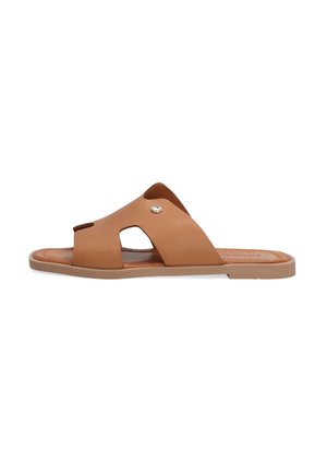 Tan leather slide sandal with an open toe, cross straps, and round cutouts. Soft insole and flat rubber sole with metal accent detail.