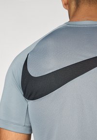 Hele hall halluxid, hingeldav mesh tekstuuriga sportlik särk, millel on must Nike logo aktsent õlal. Lühikesed varrukad.