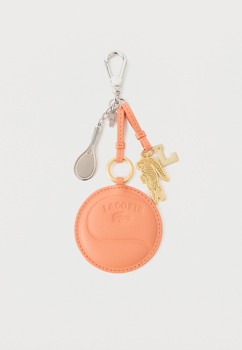 Porte-clés rond en cuir pêche embossé du logo Lacoste, attaché à un pendentif crocodile doré, un pendentif lettre "L" et un pendentif raquette de tennis argenté.