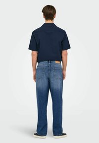 Kortermet, marineblå skjorte med teksturert stoff kombinert med lyseblå, løstsittende denimjeans. Bakvisning viser to baklommer og kant.