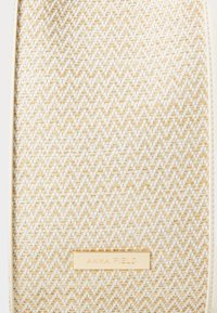 Vævet beige taske med en tekstureret overflade, der har en guld metal logo-plade. Ensfarvede hvide kanter fremhæver den rektangulære form.