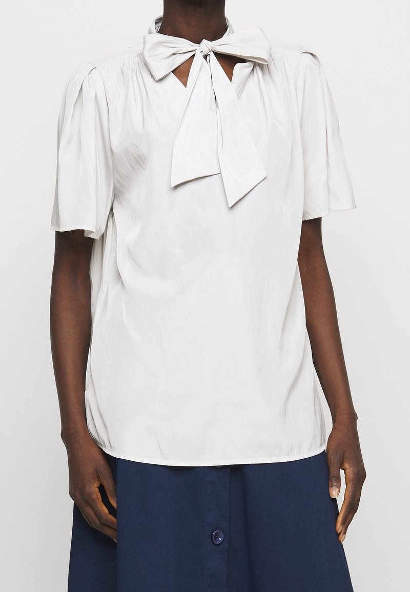 Světlá šedá blůza s krátkými nabíranými rukávy a mašlí na výstřihu; hladká textura a volný střih.