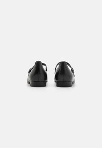 Schwarze Lederschuhe mit niedrigem Absatz, die eine abgerundete Form und seitliche Aussparungen aufweisen. Zwei dekorative Schnallen an den Riemen verleihen dem Schuh Detail.