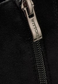 Botín de ante negro con cremallera lateral y tirador en tono plateado grabado con "WITTCHEN" y superficie de tela texturizada.